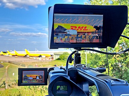 Cameraman's view of the East Midlands Airport cargo area, with a DHL cargo plane, shown on a monitor above the camera